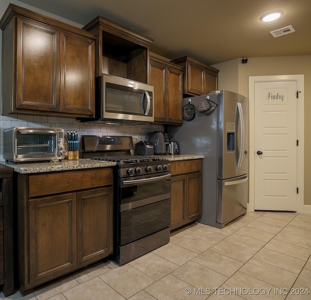 kitchen with dark brown cabinetry, decorative backsplash, light tile patterned floors, and stainless steel appliances