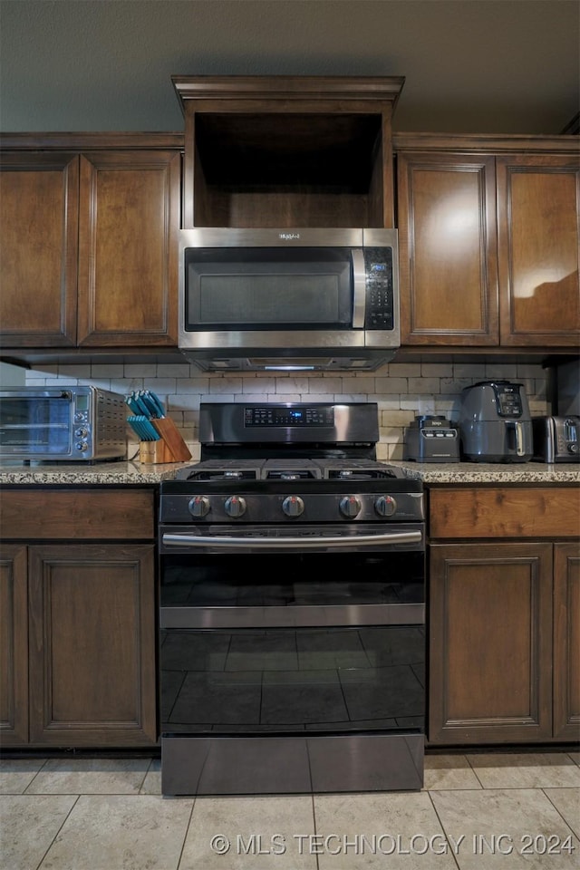 kitchen with stainless steel appliances, tasteful backsplash, light stone counters, dark brown cabinets, and light tile patterned floors