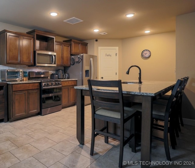 kitchen featuring decorative backsplash, appliances with stainless steel finishes, a breakfast bar area, and an island with sink