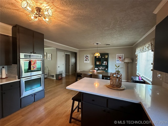 kitchen with ornamental molding, a textured ceiling, hanging light fixtures, and light hardwood / wood-style floors