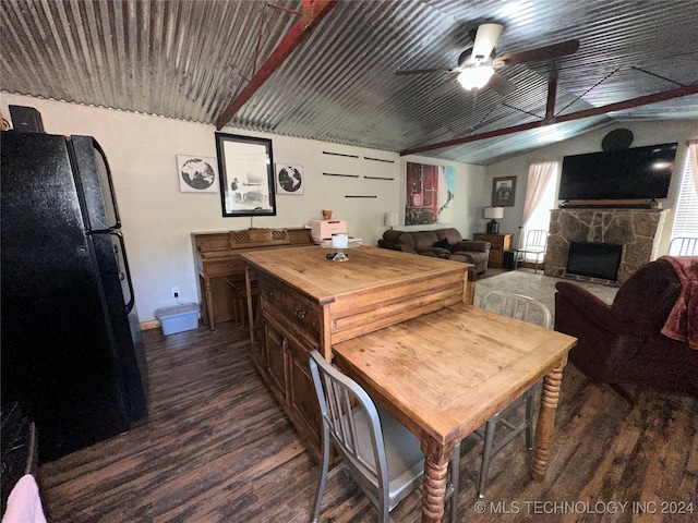 dining space with vaulted ceiling, ceiling fan, dark wood-type flooring, and a stone fireplace