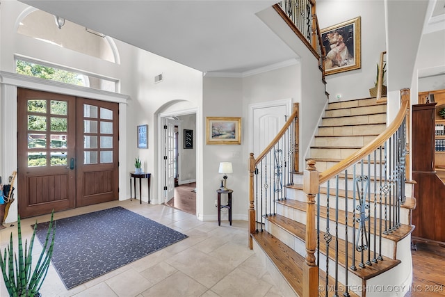 foyer featuring a towering ceiling, light tile patterned flooring, french doors, and crown molding