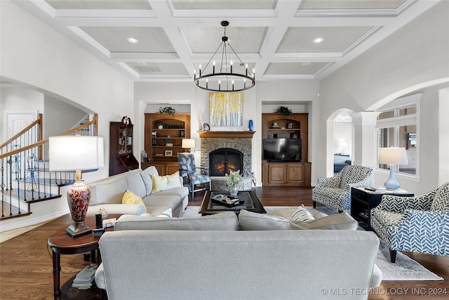 living room with coffered ceiling, a stone fireplace, dark hardwood / wood-style flooring, beamed ceiling, and an inviting chandelier