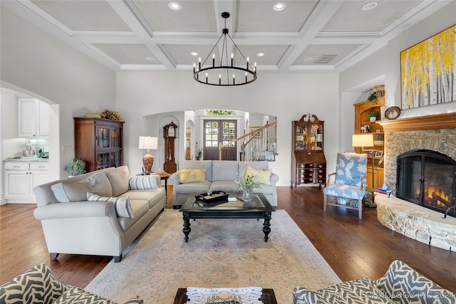 living room with coffered ceiling, a stone fireplace, dark hardwood / wood-style flooring, beam ceiling, and a chandelier