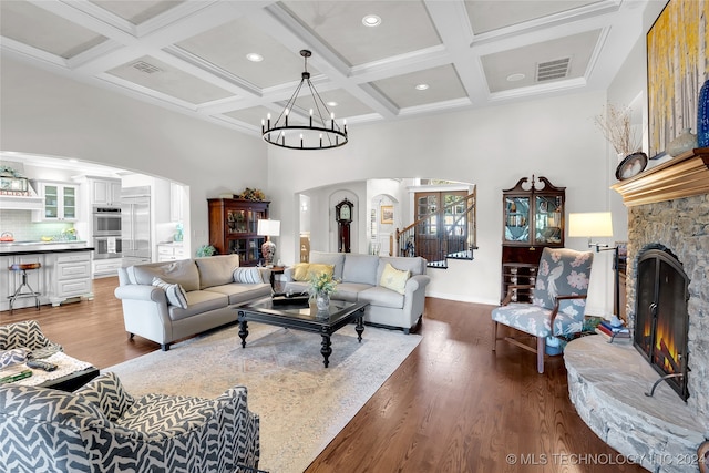 living room with a stone fireplace, hardwood / wood-style flooring, beam ceiling, and a chandelier