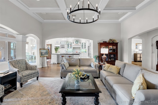 living room featuring beam ceiling, coffered ceiling, a high ceiling, an inviting chandelier, and light wood-type flooring