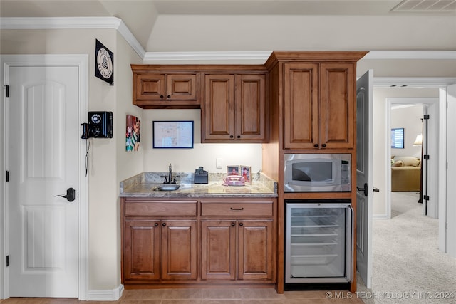 kitchen with light stone counters, beverage cooler, light colored carpet, stainless steel microwave, and crown molding