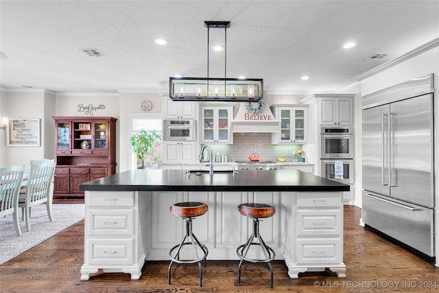 kitchen with appliances with stainless steel finishes, dark wood-type flooring, an island with sink, white cabinets, and a breakfast bar area