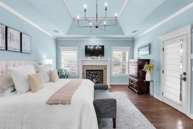 bedroom featuring an inviting chandelier, a tray ceiling, dark wood-type flooring, and a high end fireplace