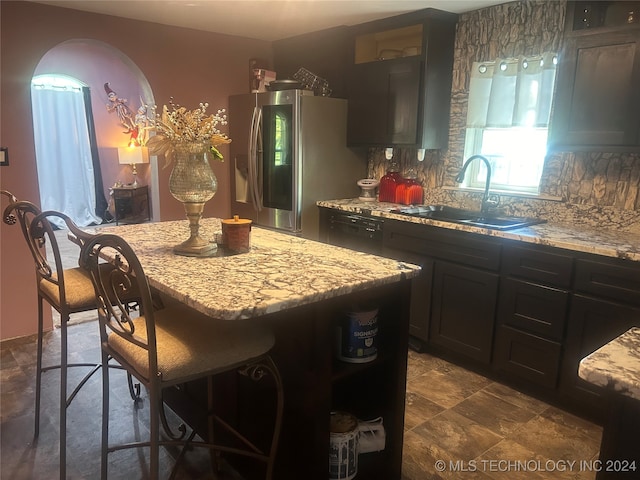 kitchen with a breakfast bar, tasteful backsplash, light stone countertops, stainless steel refrigerator with ice dispenser, and sink