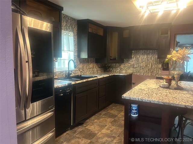 kitchen featuring light stone counters, dishwasher, dark brown cabinetry, sink, and stainless steel fridge with ice dispenser