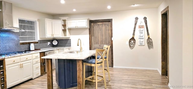 kitchen featuring light hardwood / wood-style floors, a kitchen island with sink, sink, wall chimney exhaust hood, and appliances with stainless steel finishes