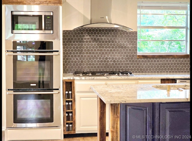 kitchen with appliances with stainless steel finishes, backsplash, wall chimney exhaust hood, and light stone countertops