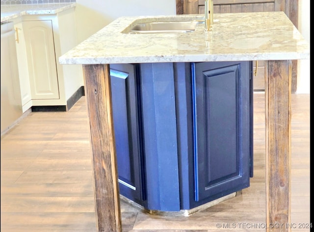 interior space with blue cabinets, an island with sink, light stone counters, light hardwood / wood-style flooring, and sink