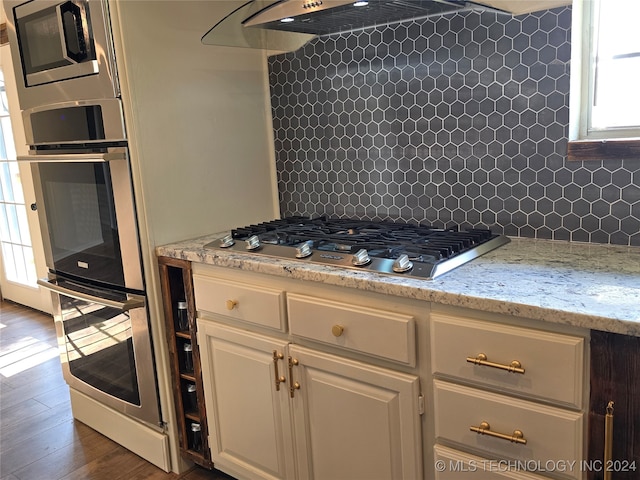 kitchen with light stone counters, tasteful backsplash, white cabinets, stainless steel appliances, and dark hardwood / wood-style flooring