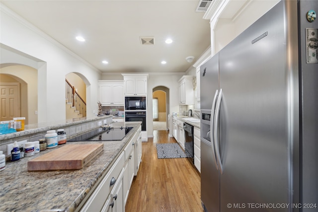 kitchen with light stone counters, white cabinetry, black appliances, light hardwood / wood-style floors, and decorative backsplash