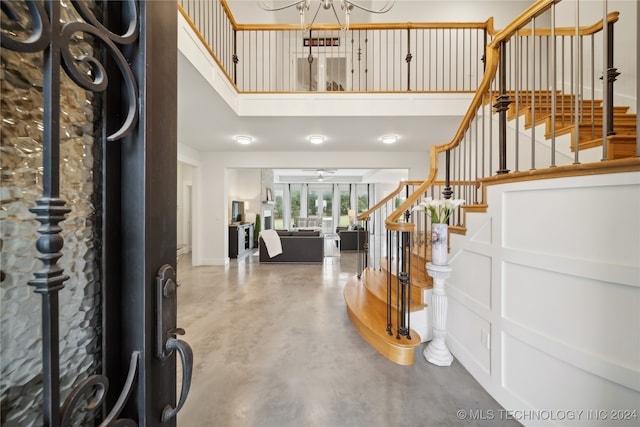 entryway with a decorative wall, ceiling fan with notable chandelier, a towering ceiling, stairs, and finished concrete floors