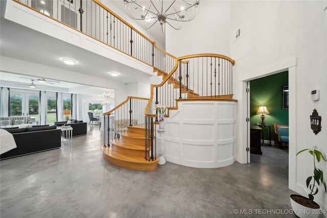 stairs featuring finished concrete flooring, a towering ceiling, visible vents, and ceiling fan with notable chandelier