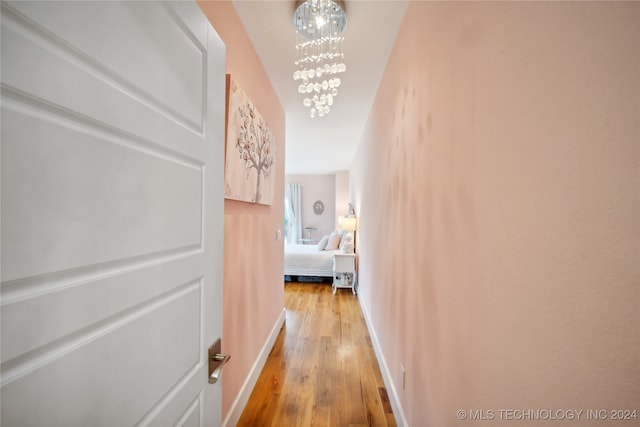 corridor featuring light wood-type flooring, baseboards, and a chandelier