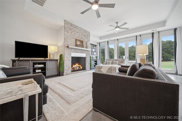 living area featuring a tray ceiling, visible vents, a fireplace, and ceiling fan