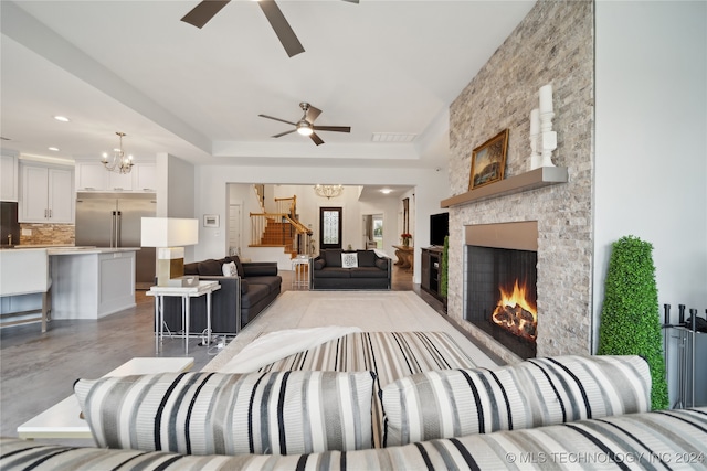 living room with ceiling fan with notable chandelier, a fireplace, finished concrete flooring, and stairs