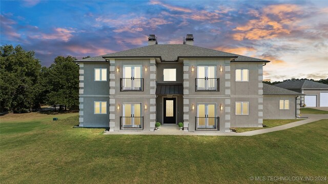 back of house with a balcony, french doors, a lawn, stucco siding, and a chimney