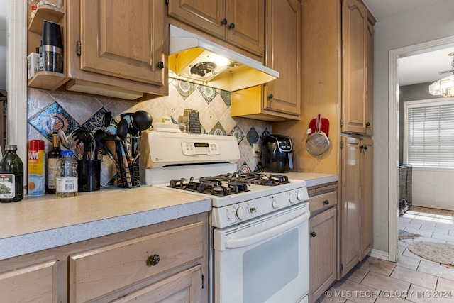 kitchen with tasteful backsplash, light tile patterned flooring, a chandelier, and gas range gas stove