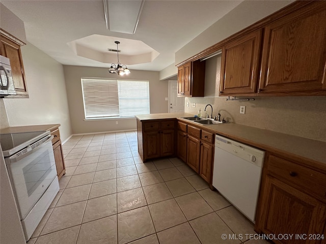 kitchen with a raised ceiling, white appliances, kitchen peninsula, pendant lighting, and an inviting chandelier