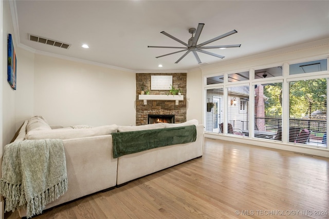 living room featuring light hardwood / wood-style floors, ceiling fan, a stone fireplace, and crown molding