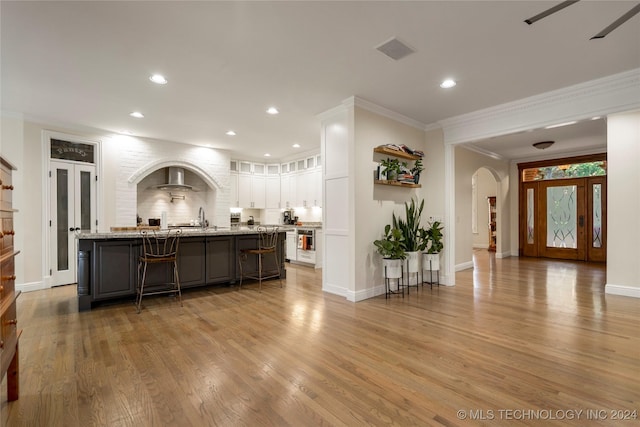 kitchen with light stone countertops, an island with sink, a kitchen bar, white cabinets, and ornamental molding