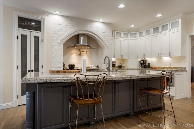 kitchen with white cabinets, light stone counters, a center island with sink, and wood-type flooring