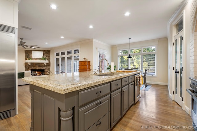 kitchen with a kitchen island with sink, stainless steel appliances, a fireplace, sink, and decorative light fixtures