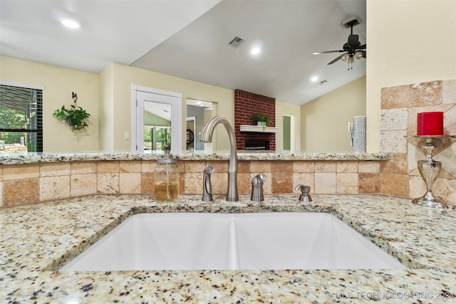 kitchen featuring ceiling fan, light stone counters, lofted ceiling, sink, and decorative backsplash