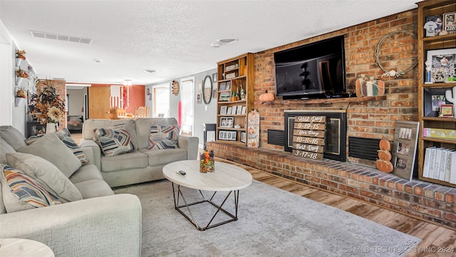 living room with a brick fireplace, a textured ceiling, and hardwood / wood-style floors