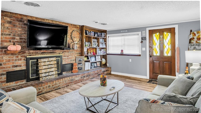 living room with a textured ceiling, hardwood / wood-style flooring, crown molding, and a brick fireplace