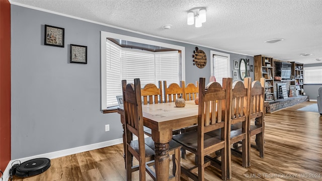 dining space featuring ornamental molding, wood-type flooring, and a textured ceiling