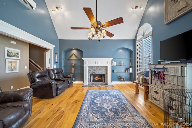 living room featuring built in shelves, a wall unit AC, ceiling fan, a fireplace, and light hardwood / wood-style floors