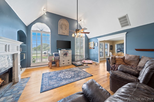 living room with vaulted ceiling, built in features, a fireplace, ceiling fan, and light hardwood / wood-style floors