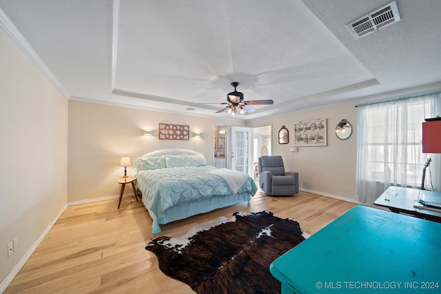 bedroom with wood-type flooring, ceiling fan, a tray ceiling, crown molding, and a textured ceiling