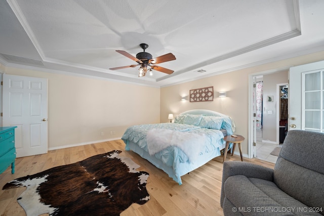 bedroom featuring ceiling fan, a walk in closet, a raised ceiling, and light wood-type flooring