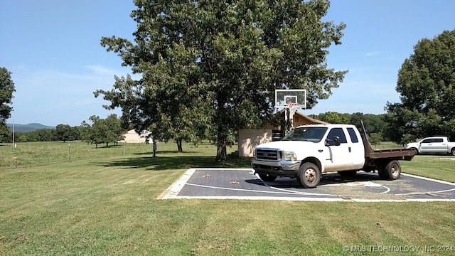 view of vehicle parking featuring basketball hoop and a yard