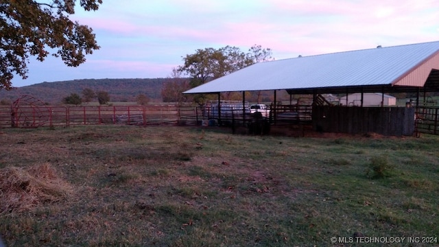 yard at dusk featuring a rural view and an outdoor structure