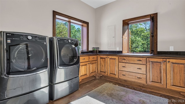 clothes washing area with a healthy amount of sunlight, washer and clothes dryer, and cabinets