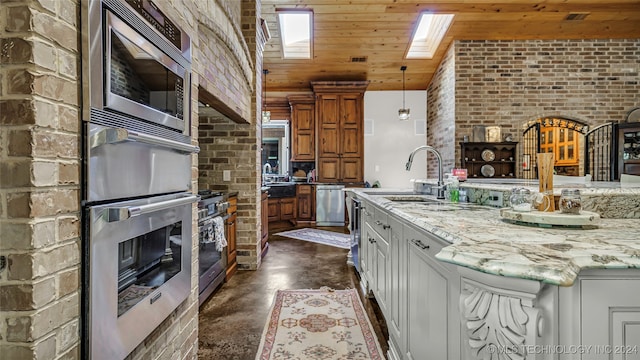 kitchen with light stone counters, sink, white cabinetry, stainless steel appliances, and a skylight