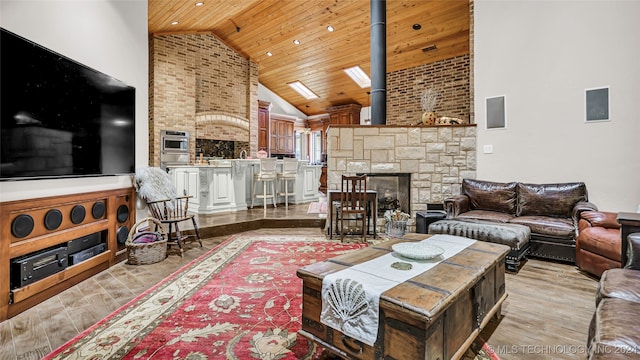 living room featuring a skylight, wood ceiling, light hardwood / wood-style flooring, high vaulted ceiling, and a fireplace