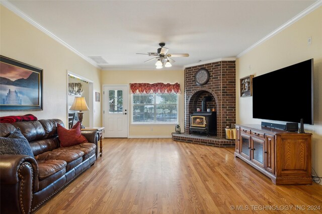 living room with ceiling fan, light hardwood / wood-style flooring, crown molding, and a wood stove