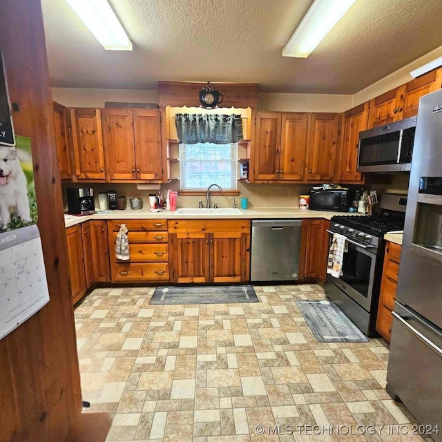 kitchen with a textured ceiling, appliances with stainless steel finishes, and sink