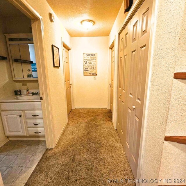 corridor featuring light carpet, a textured ceiling, and sink