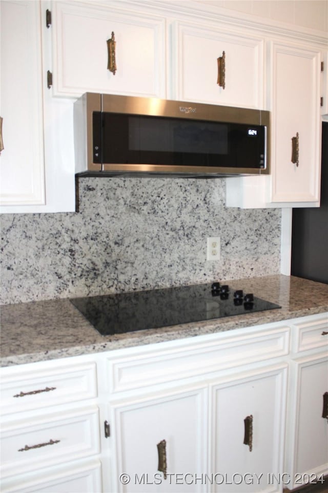 kitchen featuring tasteful backsplash, white cabinetry, light stone countertops, and black electric stovetop