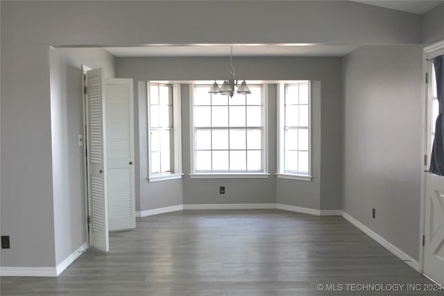 unfurnished dining area with dark wood-type flooring, a wealth of natural light, and an inviting chandelier